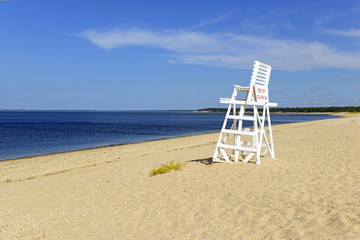 White lifeguard chair on empty sand beach with blue sky