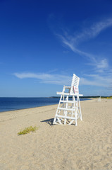 White lifeguard chair on empty sand beach with blue sky
