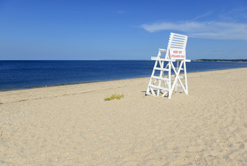 White lifeguard chair on empty sand beach with blue sky