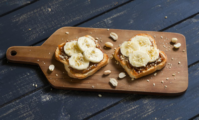 sandwich with peanut butter, banana and peanuts, served on the Board, on a wooden surface