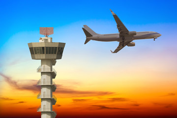 Commercial airplane flying over airport control tower at sunset