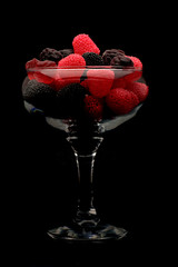 raspberries and blackberries in a beautiful glass on a black background