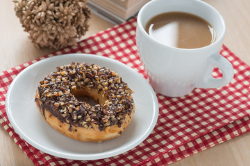 Donut chocolate with nut topping and a cup of coffee.