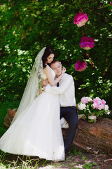 Happy young bride and groom in a pink decorated with peonies area in nature, family, relationships, romance, smiles, hugs, love, lifestyle