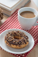 Donut chocolate with nut topping and a cup of coffee on the tabe