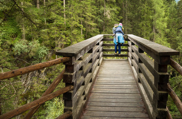 mother with baby in carrier standing on view platform and observing waterfall in krimm