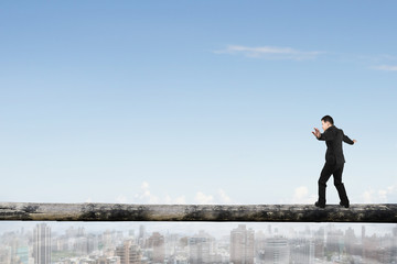 Businessman balancing on tree trunk high in the sky