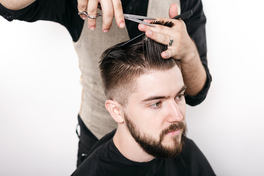 Hairdresser cuts hair of handsome satisfied client in studio