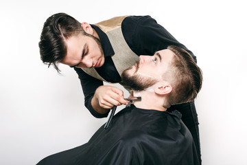 Brunette barber shaving bearded customer with razor