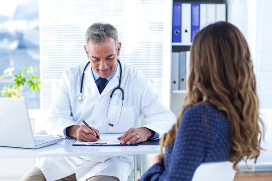 Male doctor writing prescription for woman in hospital