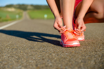 Running challenge concept. Female athlete tying sport footwear laces on road before training.