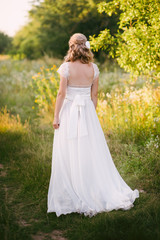 Fototapeta premium Stylish beautiful blonde bride standing in her wedding dress back to nature in the sunset light, wedding, marriage, tenderness, woman, lifestyle