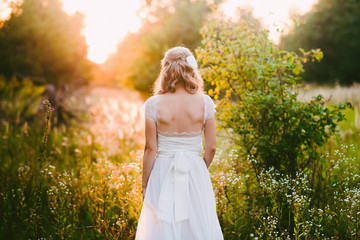 Fototapeta na wymiar Stylish beautiful blonde bride standing in her wedding dress back to nature in the sunset light, wedding, marriage, tenderness, woman, lifestyle