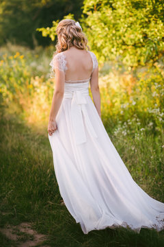 Stylish beautiful blonde bride standing in her wedding dress back to nature in the sunset light, wedding, marriage, tenderness, woman, lifestyle
