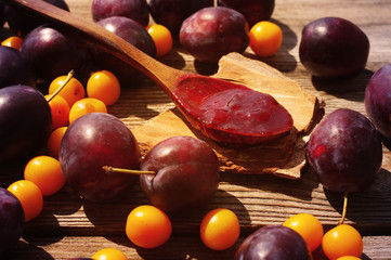 Plum jam in a wooden spoon and plums with a yellow cherry plum on a wooden surface. 