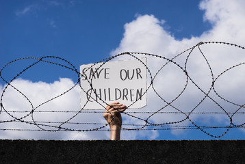 Save our children – Flüchtling hinter Stacheldraht zeigt Schild