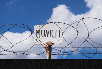 Flüchtling hinter Stacheldraht hält Schild mit Aufschrift München hoch