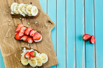 Bruschetta with cheese ricotta, strawberry and banana over wooden turquoise table