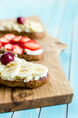 Bruschetta with cheese ricotta, berries and banana over wooden turquoise table