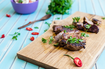 Grilled pork steak cutting on chopping board with vegetables over wooden turquoise table