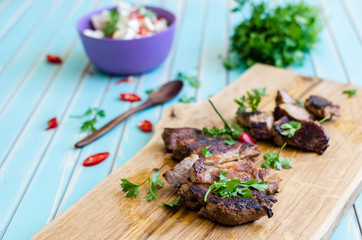 Grilled pork steak cutting on chopping board with vegetables over wooden turquoise table