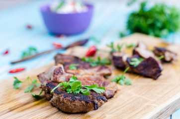 Grilled pork steak cutting on chopping board with vegetables over wooden turquoise table