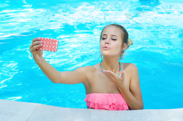 Adorable young woman blowing a kiss to her friend while communicating over the cell phone in the pool