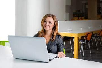 Young successful businesswoman with laptop computer at office using tablet computer or having a coffee break.