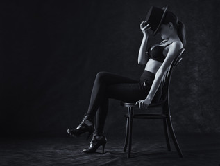 Obraz na płótnie Canvas Sexy young woman sitting on a chair on a black background.