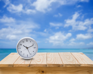 Clock on wood table with blue sea sky background