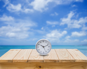 Clock on wood table with blue sea sky background