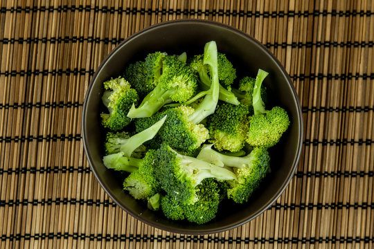 Bunch of fresh green broccoli in dark brown bowl over wooden background