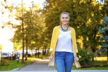 Happy young woman in yellow coat in autumn street