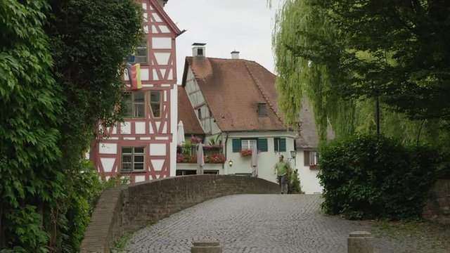 Wide shot of man walking on cobblestone bridge in village / Ulm, Germany