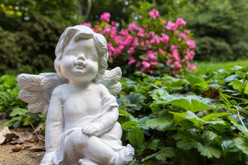 Weißer Engel Figur steht auf dem Freidhof zwischen den Blumen
