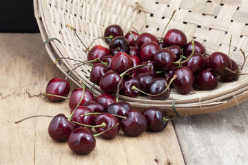 Juicy ripe cherries in bamboo basket on old wooden table top.
