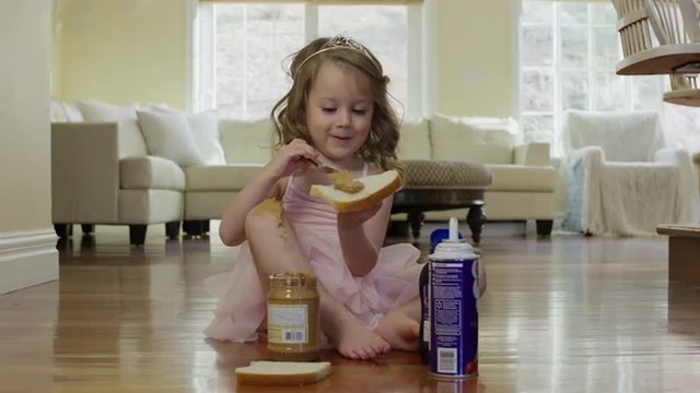 Medium shot of ballerina girl spreading peanut butter on bread / Cedar Hills, Utah, United States