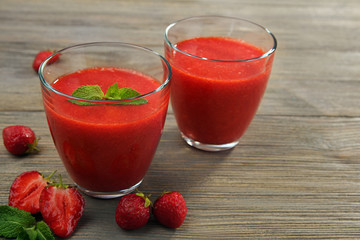 Glasses of strawberry smoothie with berries on wooden table close up