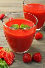 Glasses of strawberry smoothie with berries on wooden table close up