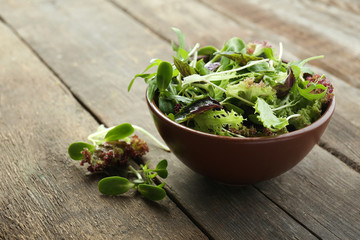 Fresh mixed green salad in bowl on wooden table close up