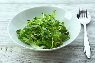Fresh mixed green salad in bowl on wooden table close up