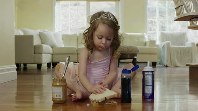 Medium shot of ballerina girl assembling sandwich on floor / Cedar Hills, Utah, United States