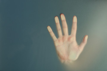 Female hand behind  wet glass, close-up