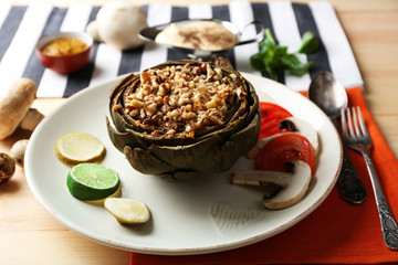 Vegetarian stuffed artichoke on plate, on table background