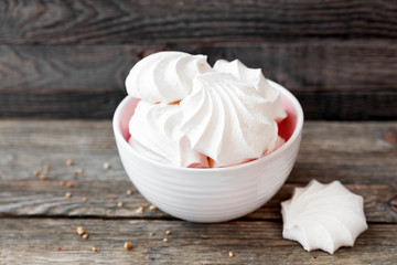 Fototapeta na wymiar Some tasty meringues lie in a white bowl on a wooden background.