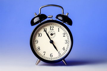 Black old fashioned alarm clock on blue background.