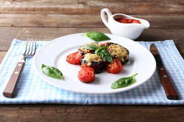 Dish of eggplant with cherry tomatoes and cheese in white plate on wooden table, closeup