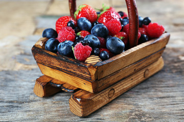 Sweet tasty berries in basket on wooden table close up