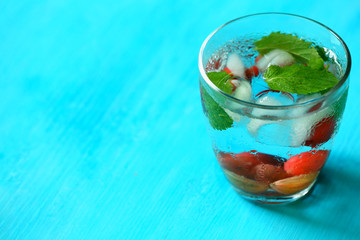 Glass of cold refreshing summer drink with berries and ice cubes on table close up
