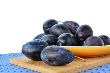 Damson plums on yellow plate over white